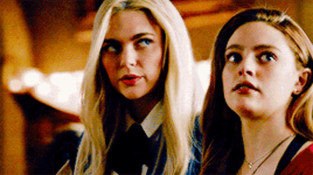 two blonde women are standing next to each other and looking up .