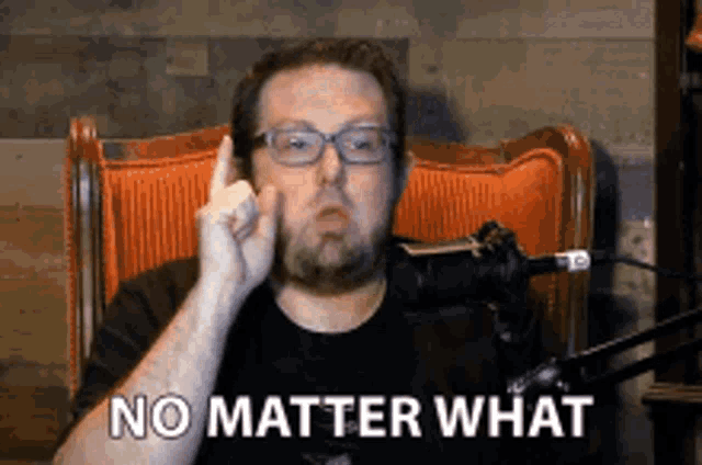 a man with glasses and a beard is sitting in a chair with the words no matter what behind him