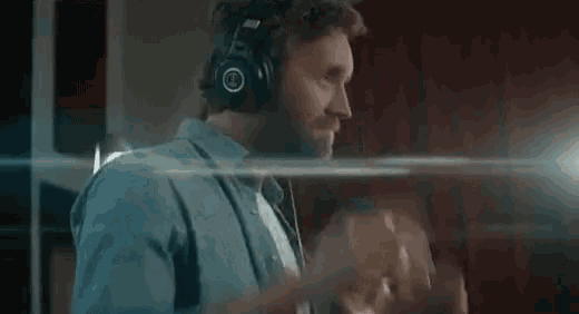 a man with a beard is wearing headphones and smiling while listening to music .
