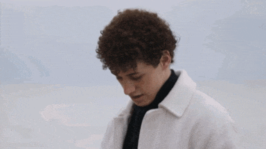 a young man with curly hair wearing a white coat and a black turtleneck