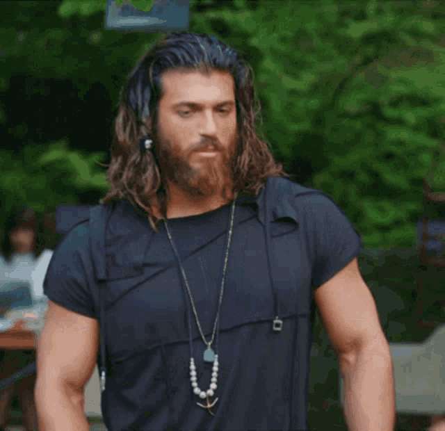 a man with long hair and a beard wearing a black shirt and a necklace