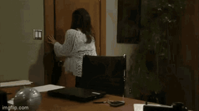 a woman is sitting at a desk with a laptop in front of her and a man is standing in the doorway behind her .