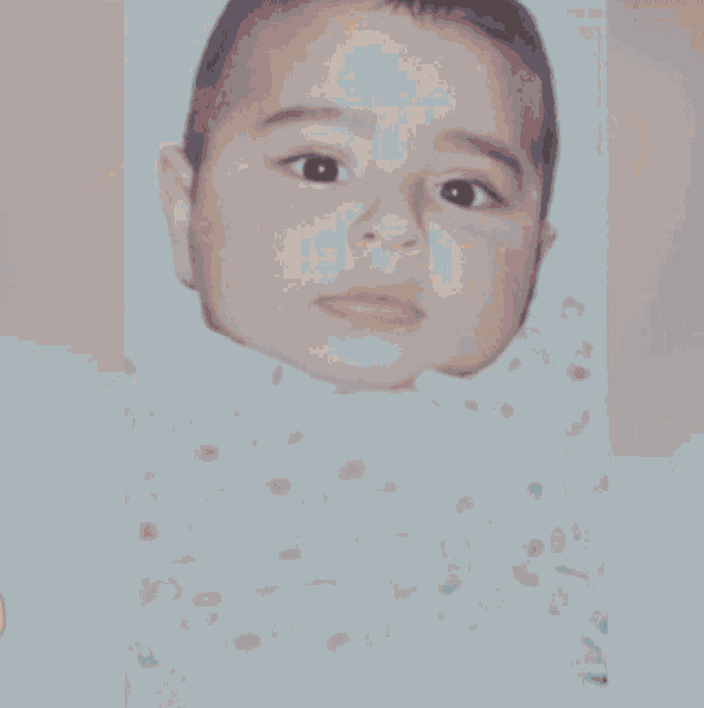a close up of a baby 's face with a pink flower in the background