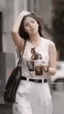 a woman in a white tank top is holding a cup of coffee .