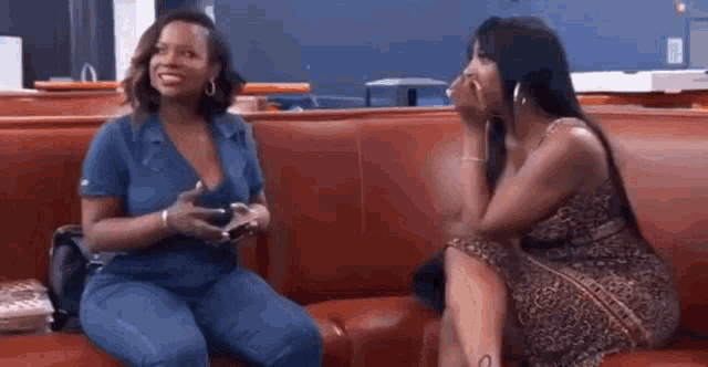 two women are sitting on a red couch talking to each other in a restaurant .