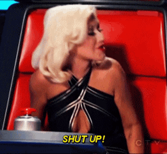 a woman in a black dress is sitting in a red chair and says " shut up "