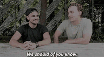 two men are sitting at a table talking to each other and one of them says `` we should of you know '' .