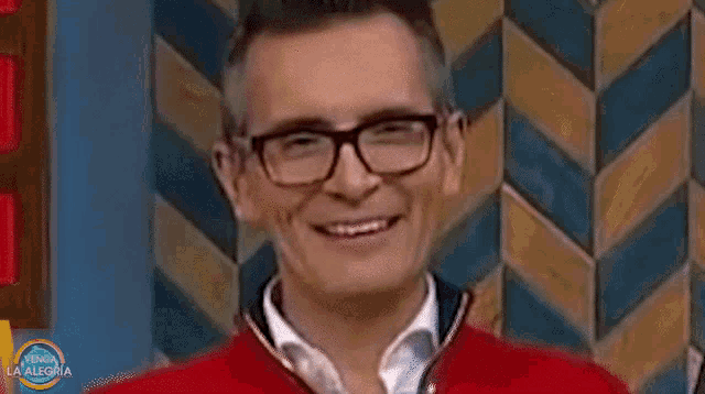 a man wearing glasses and a red jacket is laughing with his mouth open