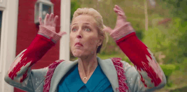 a woman in a blue shirt and a red sweater is making a funny face with her hands in the air .