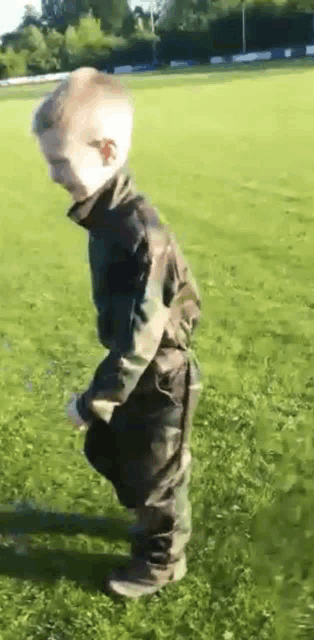 a young boy in a camouflage outfit is walking on a grassy field .