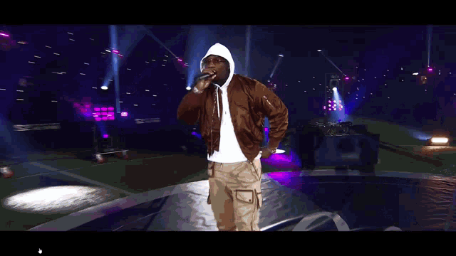 a man in a brown jacket is singing into a microphone on stage