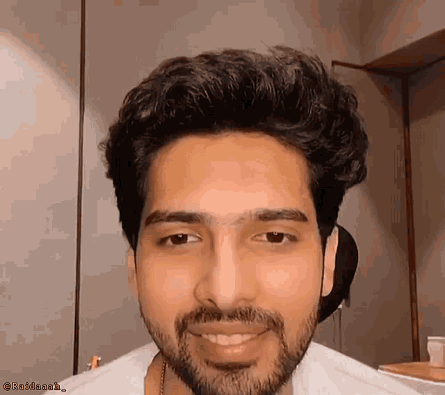 a man with a beard and a white shirt is smiling and looking at the camera ..