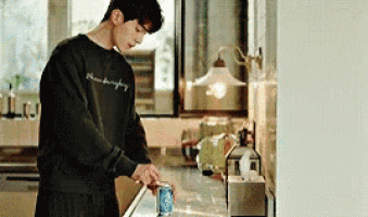 a man in a black sweatshirt is pouring a can of soda into a kitchen sink .