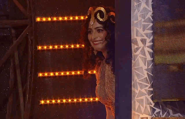 a woman in a costume with a swirl on her head looks out from behind a wall