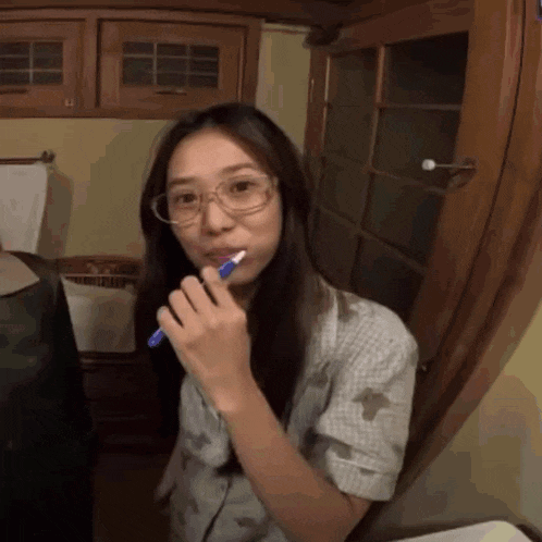 a woman wearing glasses is brushing her teeth