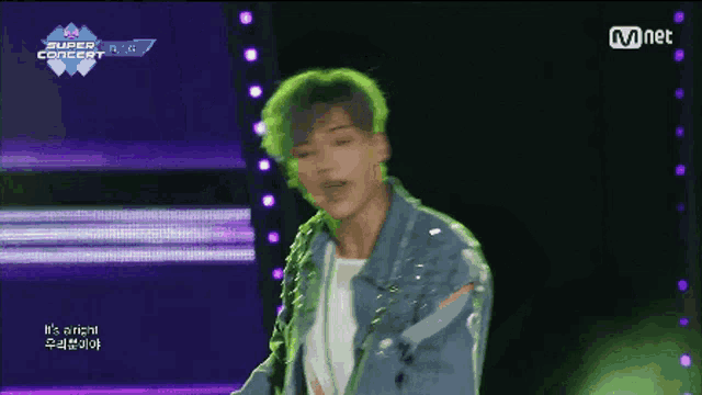 a man with green hair is dancing on a stage with a mnet logo in the background