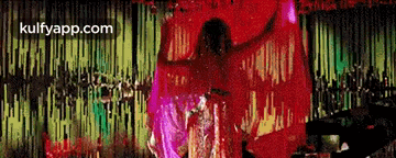 a woman in a red dress is dancing in front of a colorful background .