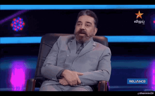a man in a suit sits in a chair with a reliance logo on the bottom of the screen