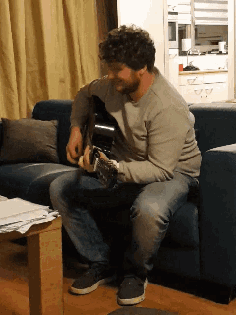 a man with curly hair is sitting on a couch playing a guitar