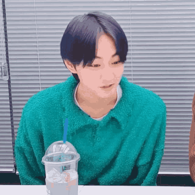 a young man with purple hair is sitting at a table with a cup of coffee and ice .