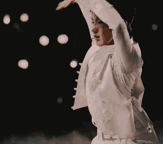 a man in a white jacket is dancing on a stage with his arms in the air .