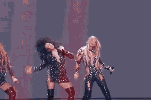 three women are dancing on a stage in front of a checkered background .