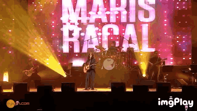 a man singing into a microphone in front of a large maris ragal sign