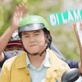 a man wearing a green helmet is riding a motorcycle while holding a sign that says dilama .