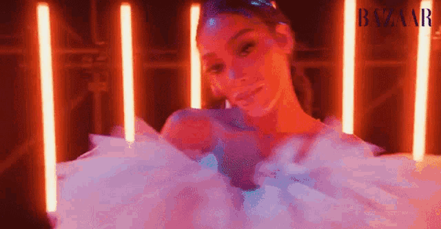 a woman in a white dress is standing in front of a neon light .