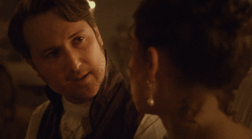 a man and a woman looking at each other with a fire in the background
