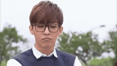 a young man wearing glasses and a white shirt is making a sad face .