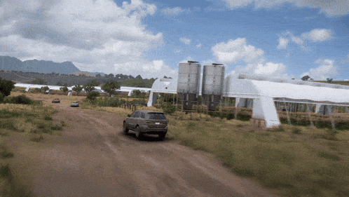a car is driving down a dirt road near a building
