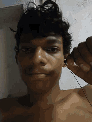 a shirtless man with curly hair is holding a pair of ear buds