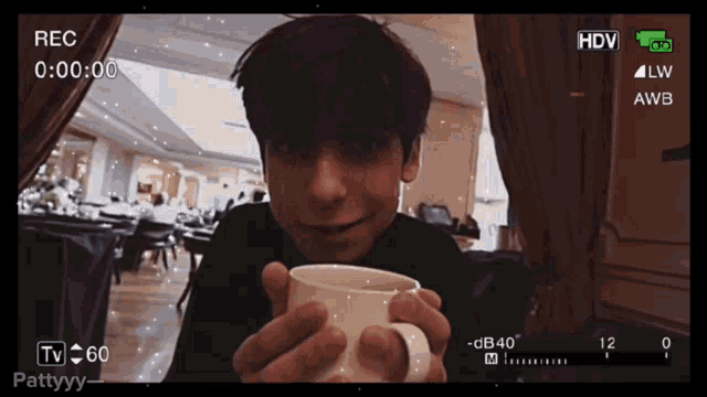 a man is holding a cup in front of a camera that says rec