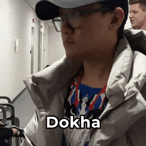 a man wearing glasses and a hat is standing in a hallway with the word dokha above him