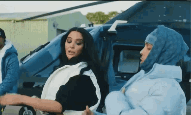 two women are standing next to each other in front of a blue helicopter .