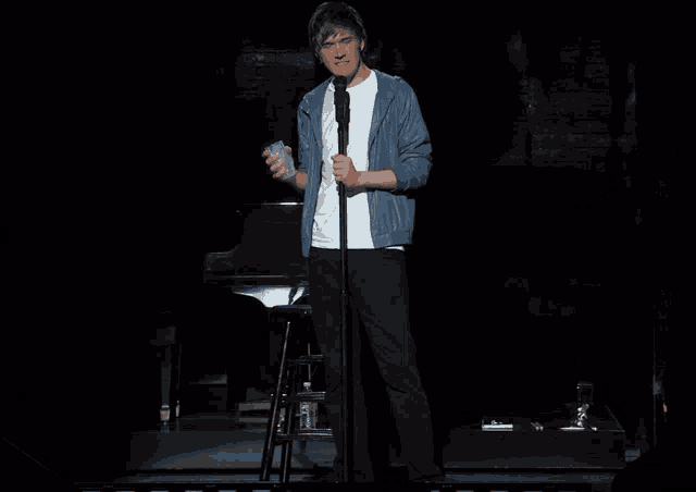 a man in a blue jacket stands in front of a microphone on a stage