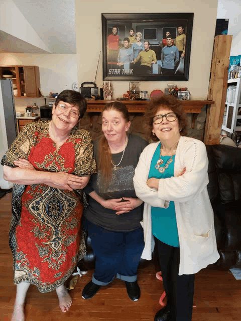three women pose for a picture in front of a star trek poster