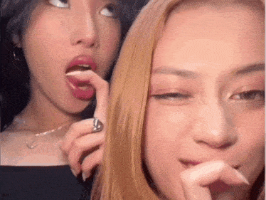 a woman with a ring on her finger is licking her lips next to another woman with a ring on her finger .
