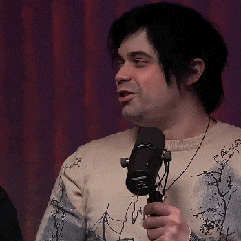 a man wearing a sweater with trees on it is holding a microphone in his hand