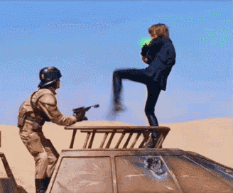 a man with a gun is standing on top of a vehicle while another man kicks him