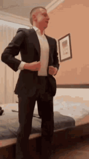 a man in a suit is standing in front of a bed adjusting his jacket .