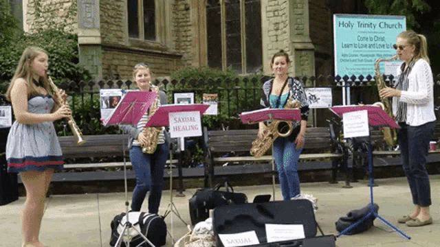 a group of women playing saxophones in front of a holy trinity church sign
