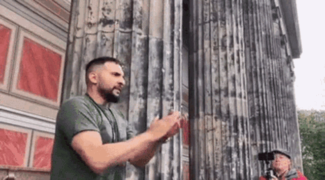 a man with a beard is standing in front of a building talking .