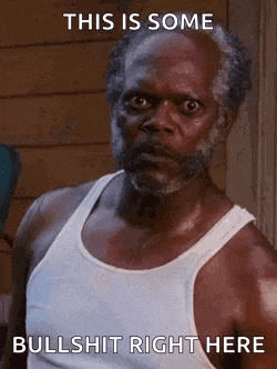 a man with a beard and a white tank top is standing in front of a building and making a funny face .