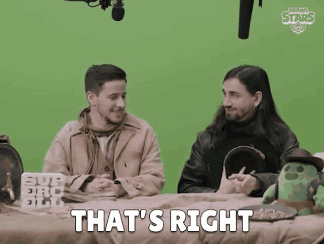two men are sitting at a table with a stuffed animal and a microphone .