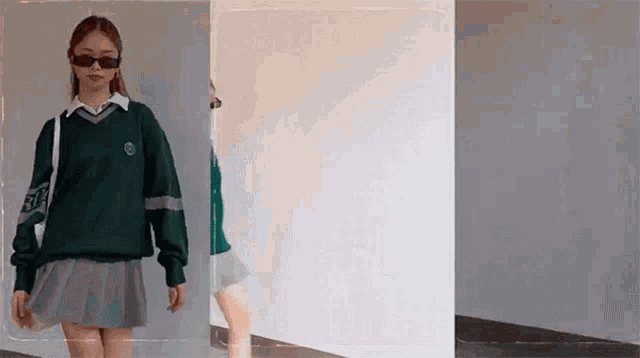 a woman wearing a green sweater and a grey skirt is standing in front of a white wall .