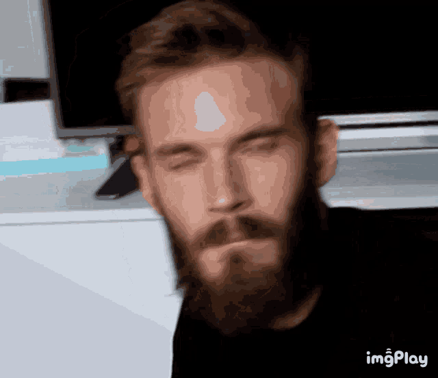 a man with a beard has his eyes closed in front of a tv and a screen that says imgplay on it