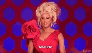 a drag queen in a red dress is standing in front of a polka dot background and saying thank you .