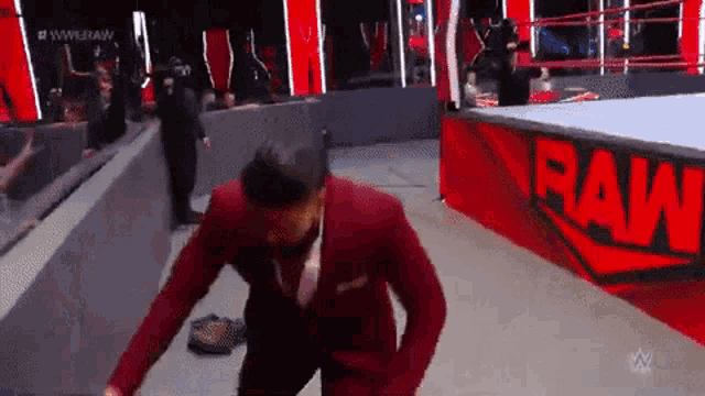 a man in a red suit is standing in front of a wrestling ring that says raw